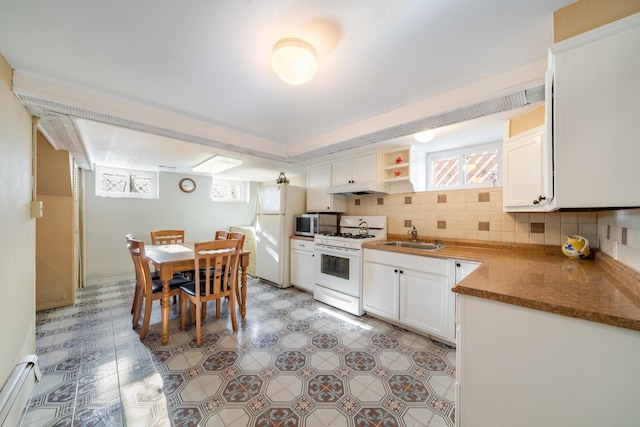 kitchen featuring white appliances, a sink, under cabinet range hood, baseboard heating, and healthy amount of natural light