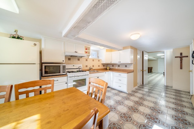 kitchen featuring white appliances, a sink, white cabinets, under cabinet range hood, and backsplash