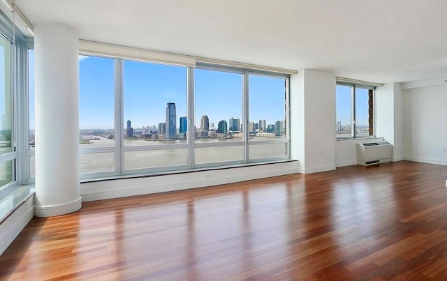 30 W St Unit 20F, New York City, NY 10004 - empty room featuring wood finished floors, a skyline view, a wall mounted AC, and ornate columns