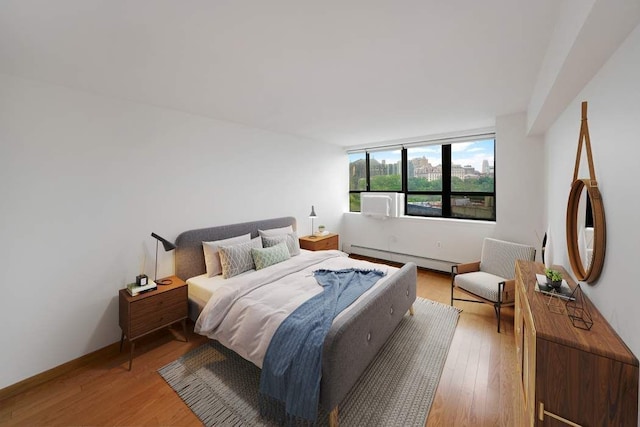 bedroom with a baseboard radiator, light wood-style flooring, and baseboards