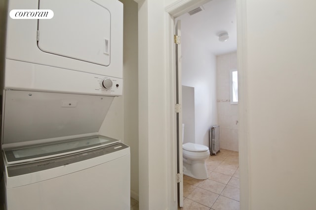 laundry area with estacked washer and dryer, radiator, and light tile patterned floors