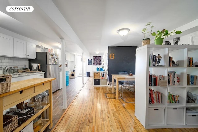 kitchen with freestanding refrigerator, a sink, light wood-style flooring, white cabinetry, and tasteful backsplash