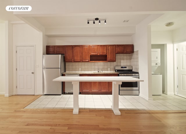kitchen with stainless steel appliances, stacked washer / drying machine, light countertops, light wood-style flooring, and backsplash