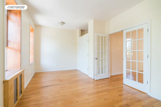 spare room featuring light wood finished floors, french doors, and baseboards