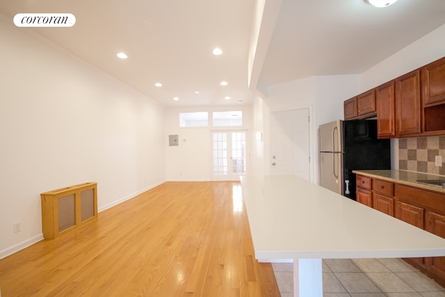 kitchen featuring light countertops, freestanding refrigerator, a kitchen island, backsplash, and brown cabinetry