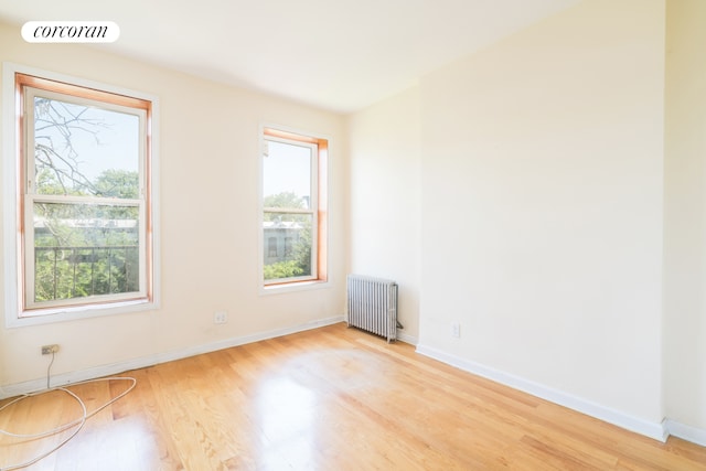 spare room with radiator, light wood-style floors, and baseboards