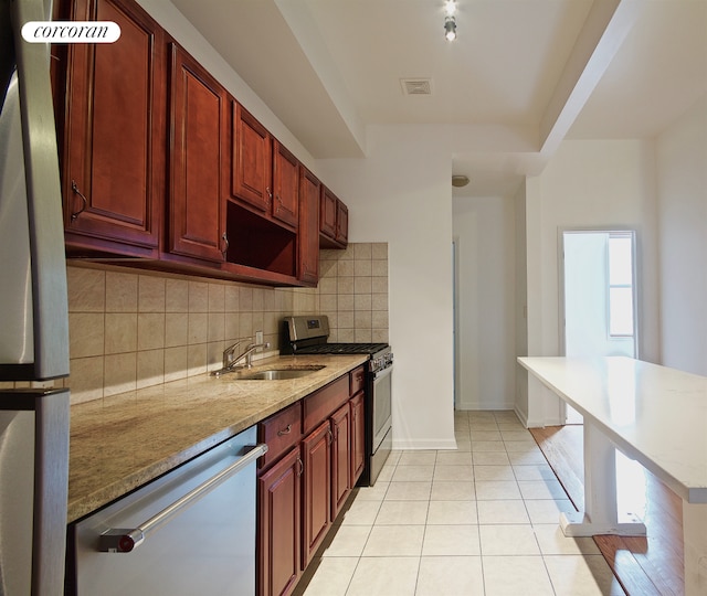 kitchen featuring appliances with stainless steel finishes, a sink, decorative backsplash, light tile patterned floors, and light stone countertops