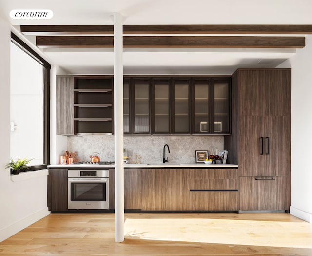 indoor wet bar with appliances with stainless steel finishes, backsplash, beam ceiling, light wood finished floors, and baseboards