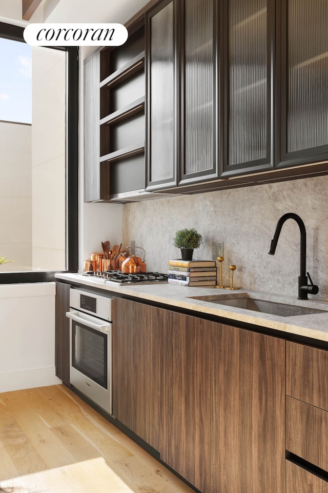 kitchen with stainless steel appliances, a sink, tasteful backsplash, and light wood-style floors