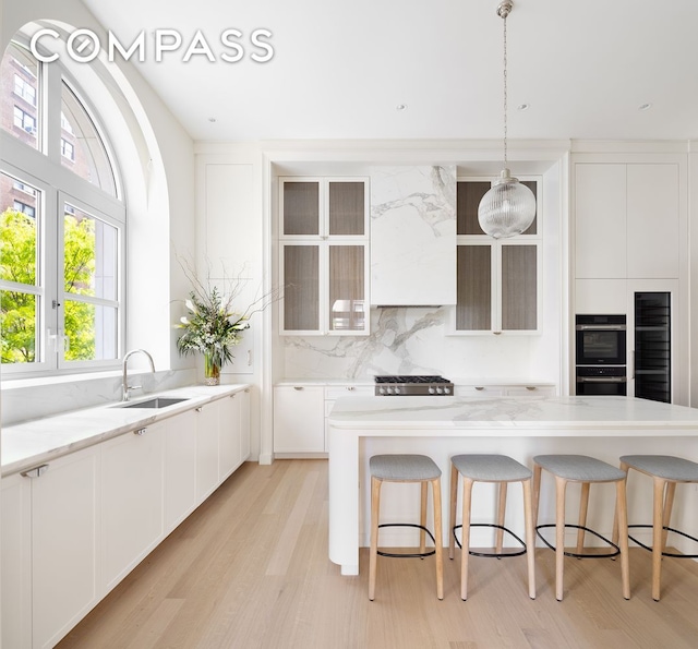 kitchen featuring light wood-type flooring, a sink, a breakfast bar, and multiple ovens