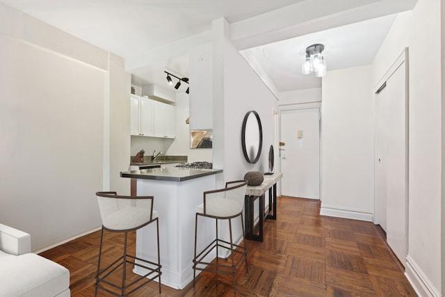 288 Lexington Ave Unit 6C, New York City, NY 10016 - kitchen with a kitchen breakfast bar, dark countertops, white cabinets, a peninsula, and baseboards