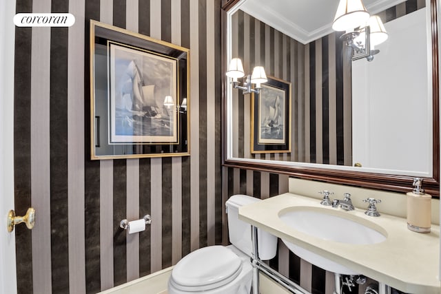 bathroom featuring wallpapered walls, crown molding, a sink, and toilet