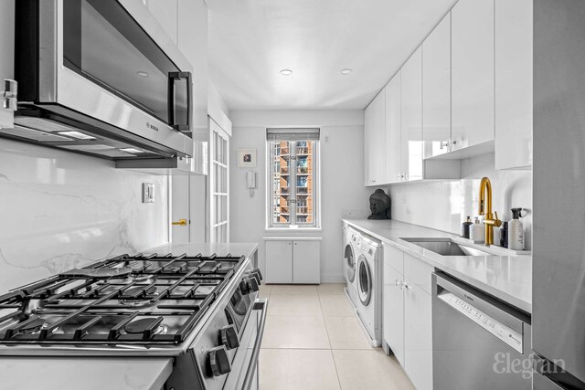 166 E 63rd St Unit 20A, New York City, NY 10065 - kitchen featuring appliances with stainless steel finishes, a sink, white cabinets, separate washer and dryer, and recessed lighting