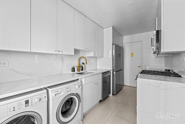 166 E 63rd St Unit 20A, New York City, NY 10065 - kitchen with stainless steel appliances, separate washer and dryer, a sink, white cabinetry, and light tile patterned flooring