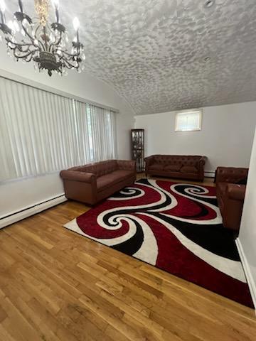 10567 Flatlands 7th St, New York City, NY 11236 - living room featuring a chandelier, wood finished floors, vaulted ceiling, and baseboard heating