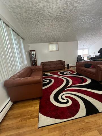 10567 Flatlands 7th St, New York City, NY 11236 - living room featuring light wood-type flooring, a baseboard heating unit, and a textured ceiling