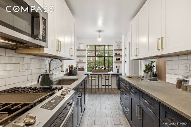 116 Pinehurst Ave Unit H32, New York City, NY 10033 - kitchen featuring appliances with stainless steel finishes, open shelves, white cabinetry, a sink, and ornamental molding