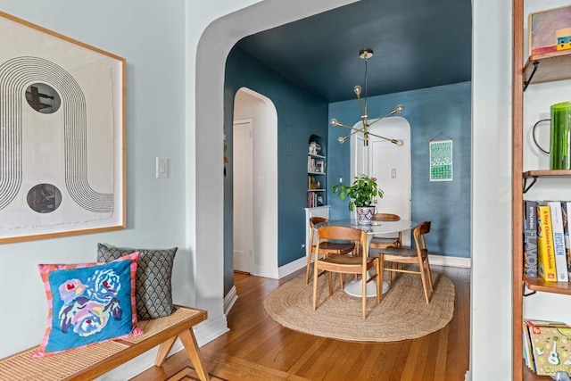 dining space with wood finished floors, arched walkways, a chandelier, and baseboards