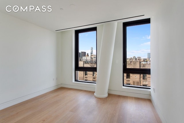 242 Broome St Unit 7D, New York City, NY 10002 - empty room with light wood-style flooring, a city view, and baseboards