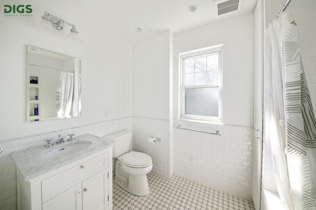 685 E 22nd St, New York City, NY 11210 - full bath with tile walls, toilet, vanity, wainscoting, and tile patterned flooring