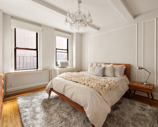 74 W 68th St Unit 7F, New York City, NY 10023 - bedroom featuring light wood-style floors, a chandelier, beam ceiling, and baseboards