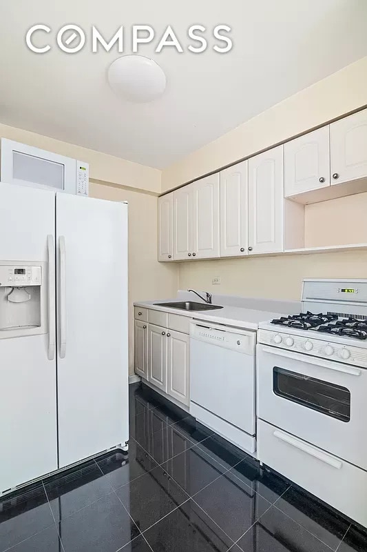 153 E 57th St Unit 17F, New York City, NY 10022 - kitchen featuring white appliances, a sink, white cabinetry, light countertops, and dark tile patterned flooring