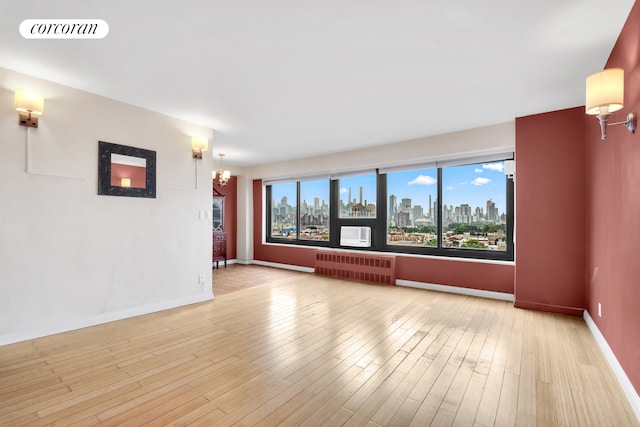 33-43 14th St Unit 12B, New York City, NY 11106 - empty room featuring radiator, a skyline view, baseboards, and wood finished floors