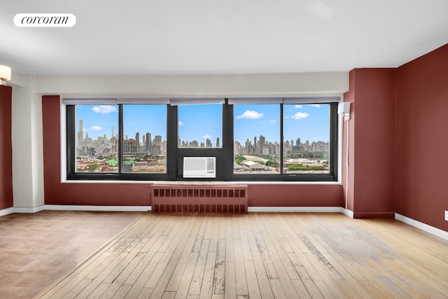 33-43 14th St Unit 12B, New York City, NY 11106 - unfurnished room with radiator, a view of skyline, hardwood / wood-style floors, and healthy amount of natural light