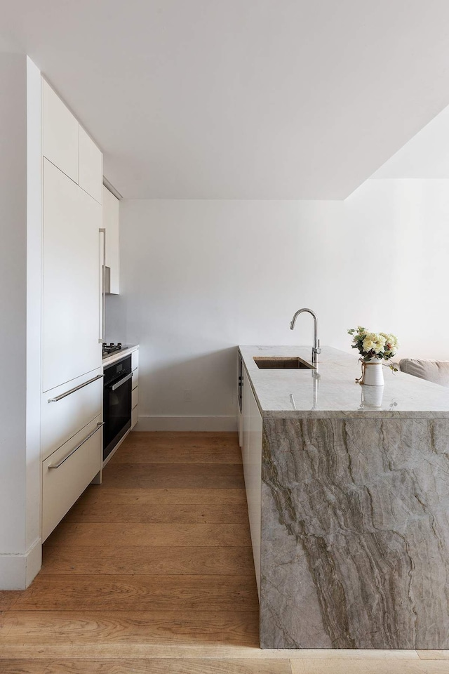 15 W 61st St Unit 12G, New York City, NY 10023 - kitchen featuring a sink, white cabinetry, modern cabinets, light wood-style floors, and light stone counters