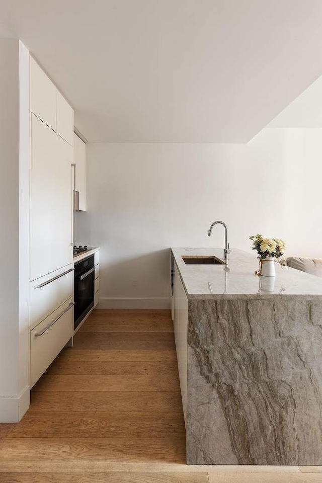 15 W 61st St Unit 12G, New York City, NY 10023 - kitchen with a sink, modern cabinets, white cabinets, light wood-style flooring, and light stone counters