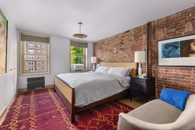 15 Jones St Unit 6A, New York City, NY 10014 - bedroom with radiator heating unit, brick wall, baseboards, and wood finished floors