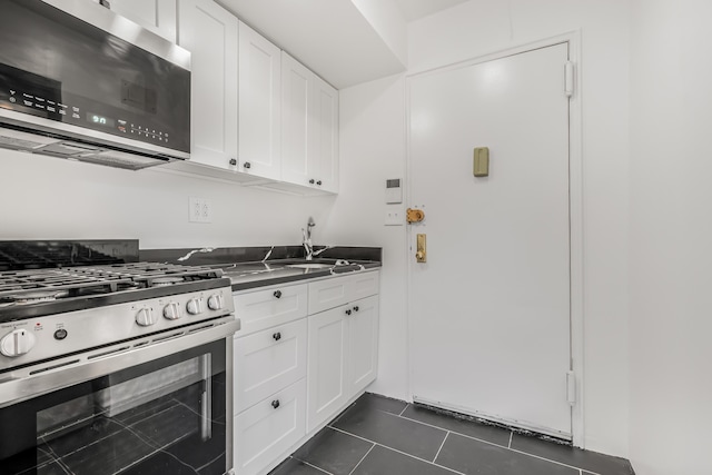 295 Bennett Ave Unit 7C, New York City, NY 10040 - kitchen featuring appliances with stainless steel finishes, dark tile patterned flooring, a sink, white cabinetry, and dark countertops