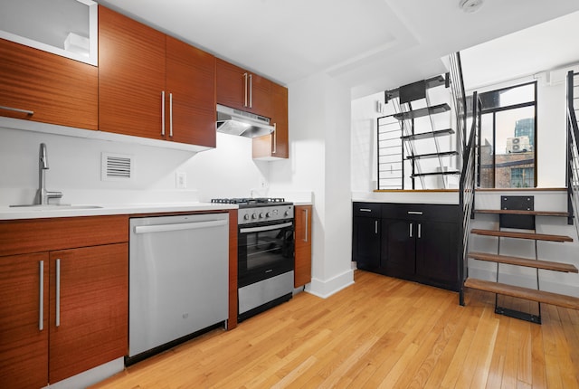 184 Thompson St Unit 5B, New York City, NY 10012 - kitchen with stainless steel appliances, a sink, under cabinet range hood, light wood-type flooring, and brown cabinetry