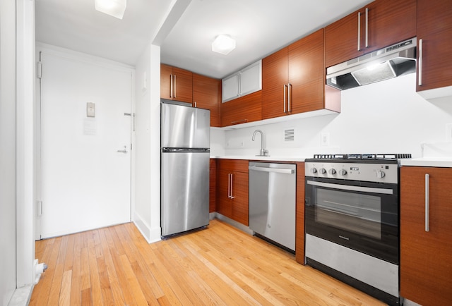 184 Thompson St Unit 5B, New York City, NY 10012 - kitchen with appliances with stainless steel finishes, under cabinet range hood, light countertops, brown cabinetry, and light wood-style flooring