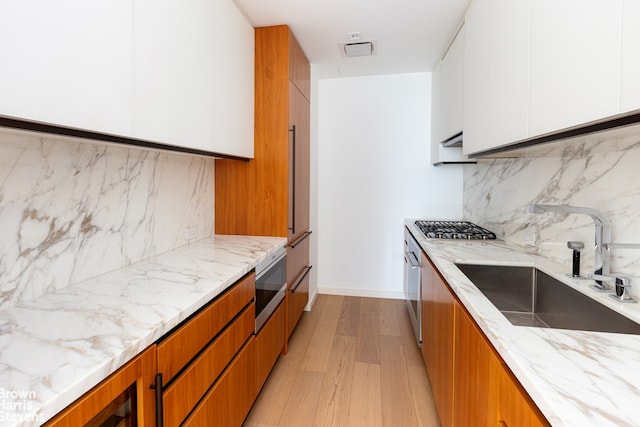 1 W End Ave Unit 18H, New York City, NY 10023 - kitchen featuring a sink, light stone counters, modern cabinets, white cabinetry, and light wood-style floors