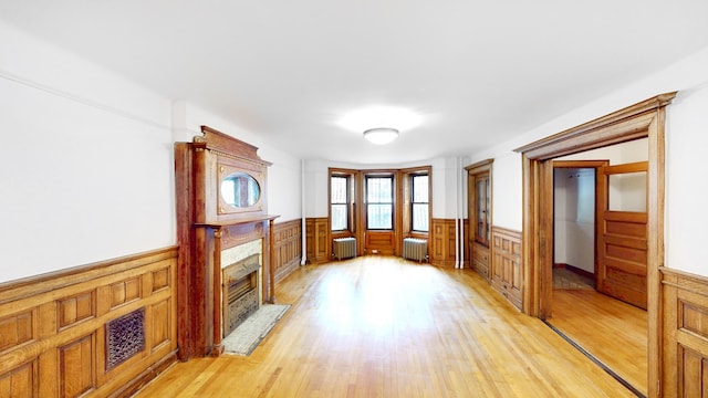 93A Rutland Rd, New York City, NY 11225 - unfurnished living room featuring radiator, wainscoting, light wood-style flooring, a high end fireplace, and wood walls
