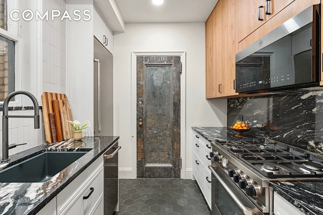 40 W 67th St Unit 1A, New York City, NY 10023 - kitchen with stainless steel appliances, a sink, dark stone counters, dark tile patterned flooring, and tasteful backsplash