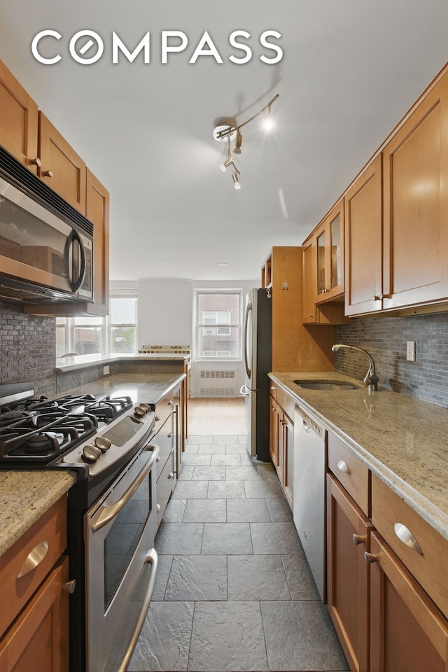 400 E 17th St Unit 711, New York City, NY 11226 - kitchen with appliances with stainless steel finishes, brown cabinetry, tasteful backsplash, radiator heating unit, and stone tile flooring