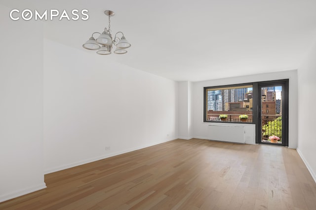 201 W 70th St Unit 8L, New York City, NY 10023 - unfurnished room featuring a chandelier, light wood-style flooring, baseboards, and radiator heating unit