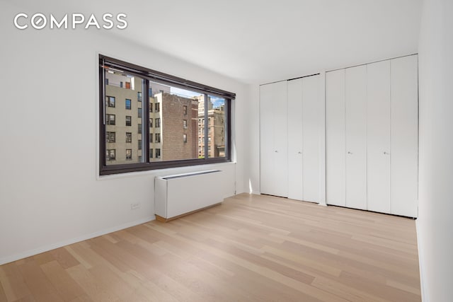 201 W 70th St Unit 8L, New York City, NY 10023 - unfurnished bedroom with wood finished floors, radiator, and two closets