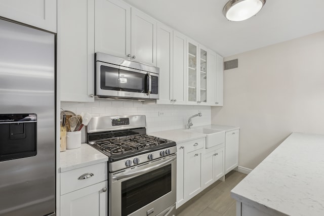 315 E 70th St Unit 9A, New York City, NY 10021 - kitchen with stainless steel appliances, a sink, glass insert cabinets, decorative backsplash, and white cabinetry
