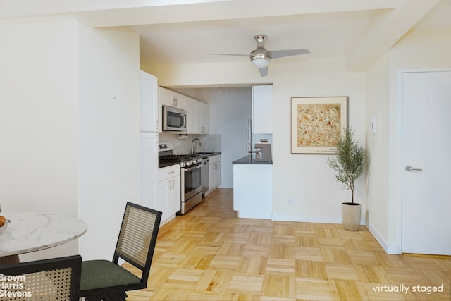 249 E 48th St Unit 3A, New York City, NY 10017 - kitchen featuring appliances with stainless steel finishes, tasteful backsplash, white cabinets, ceiling fan, and baseboards