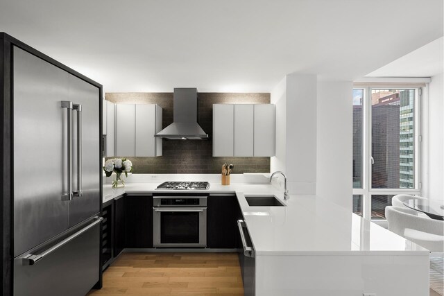 247 W 46th St Unit 3505, New York City, NY 10036 - kitchen with appliances with stainless steel finishes, wall chimney exhaust hood, light wood-style floors, light countertops, and a peninsula