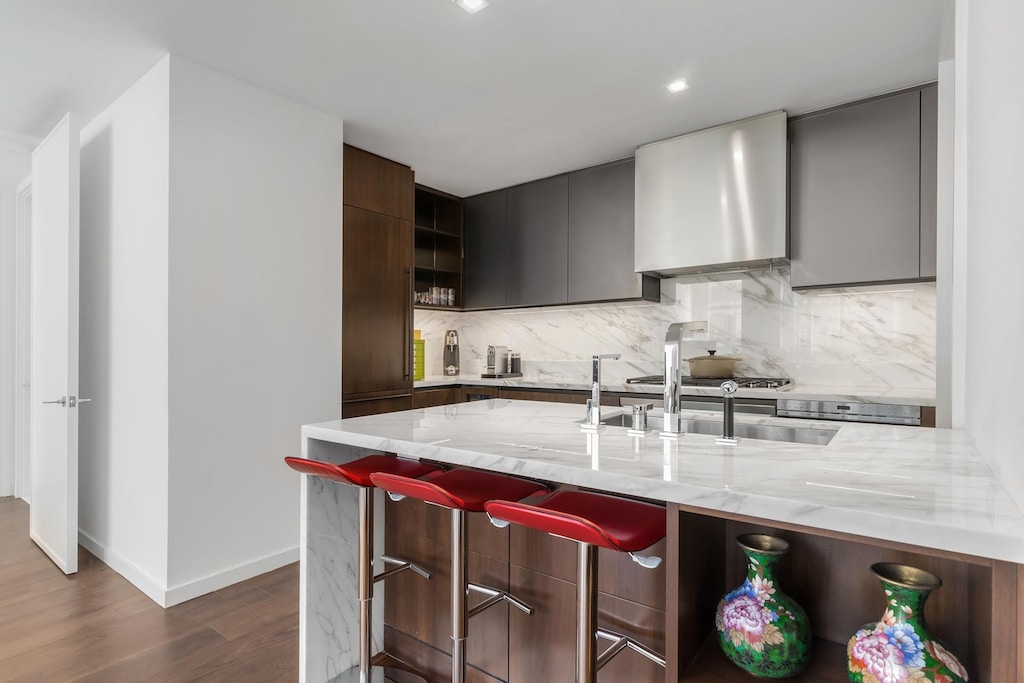 1 W End Ave Unit 14E, New York City, NY 10023 - kitchen featuring wall chimney range hood, light stone countertops, dark wood finished floors, decorative backsplash, and modern cabinets