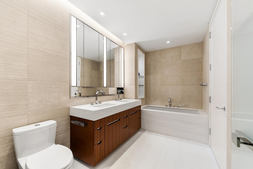 1 W End Ave Unit 14E, New York City, NY 10023 - full bathroom featuring double vanity, a bath, toilet, tile walls, and tile patterned floors