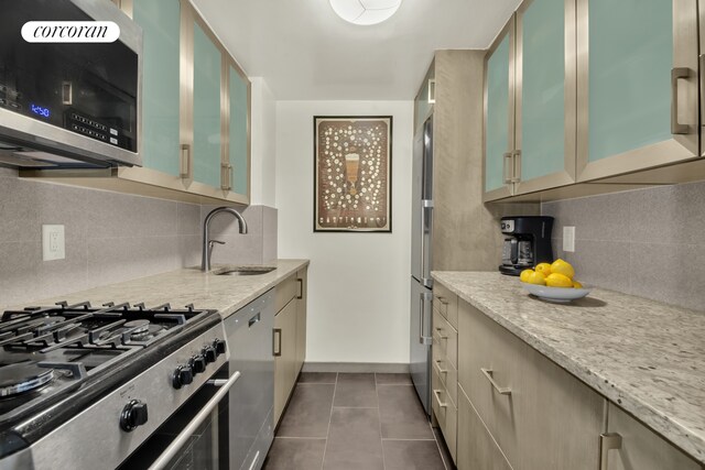 200 E 58th St Unit 5E, New York City, NY 10022 - kitchen with appliances with stainless steel finishes, decorative backsplash, light stone counters, and dark tile patterned flooring