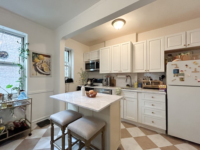 100 Bennett Ave Unit 4B, New York City, NY 10033 - kitchen with appliances with stainless steel finishes, light floors, a sink, a breakfast bar area, and white cabinetry