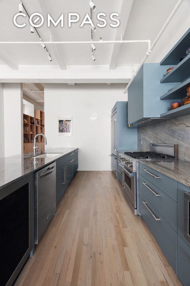 28 W 38th St Unit 6E, New York City, NY 10018 - kitchen with appliances with stainless steel finishes, a sink, dark stone counters, light wood finished floors, and rail lighting