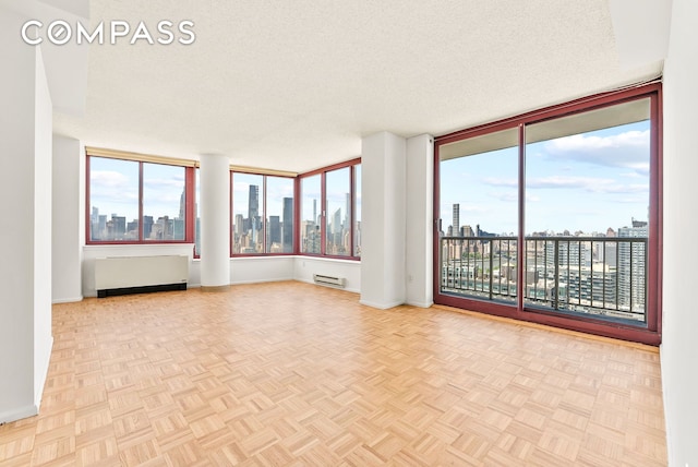 4-74 48th Ave Unit Ph2B, New York City, NY 11109 - empty room with a skyline view, radiator heating unit, baseboards, and a textured ceiling