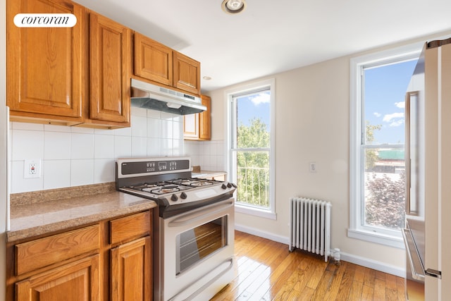 238 26th St, New York City, NY 11232 - kitchen featuring radiator heating unit, appliances with stainless steel finishes, under cabinet range hood, light wood-type flooring, and baseboards